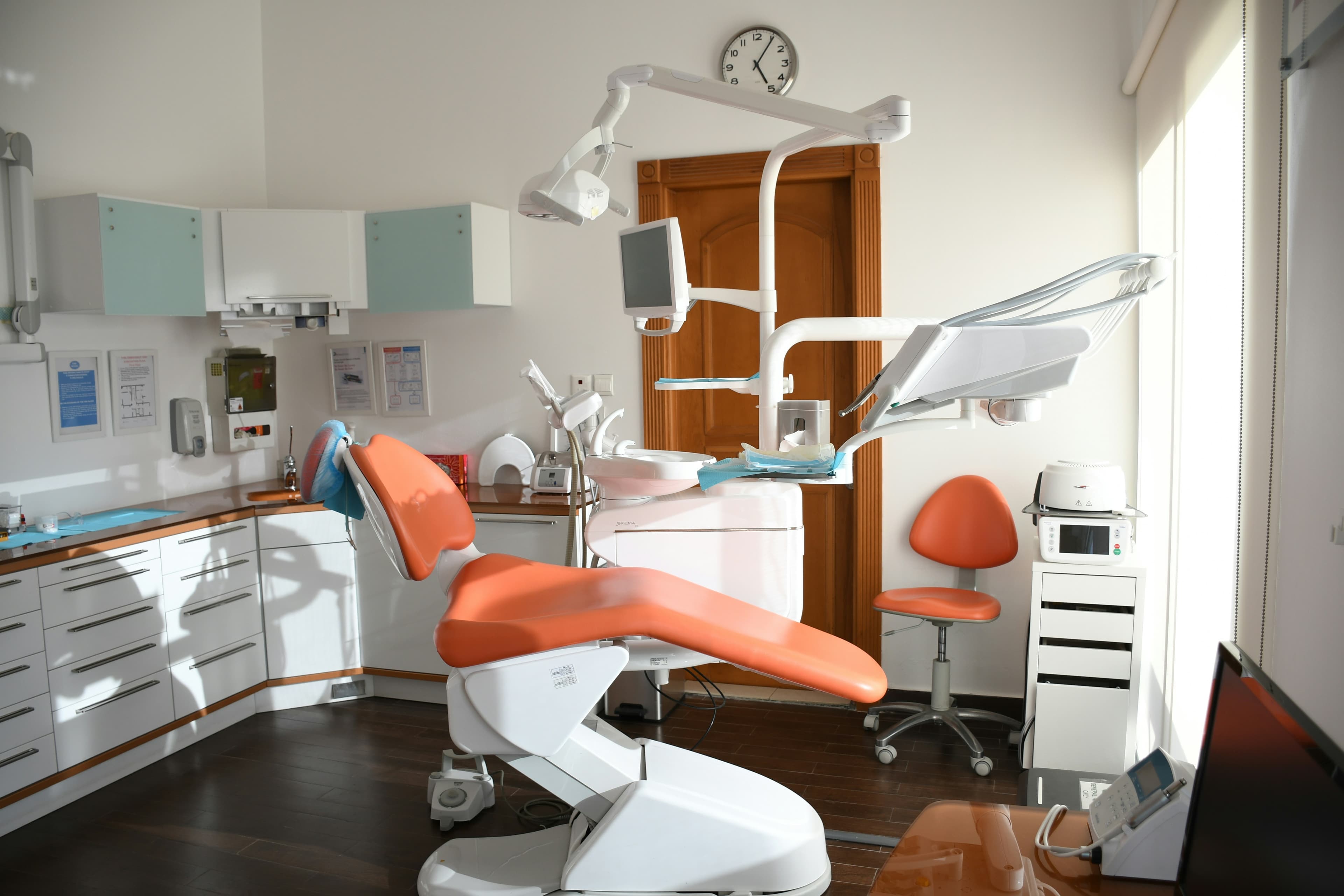 Modern dental office with an orange examination chair, medical equipment, and white storage cabinets.