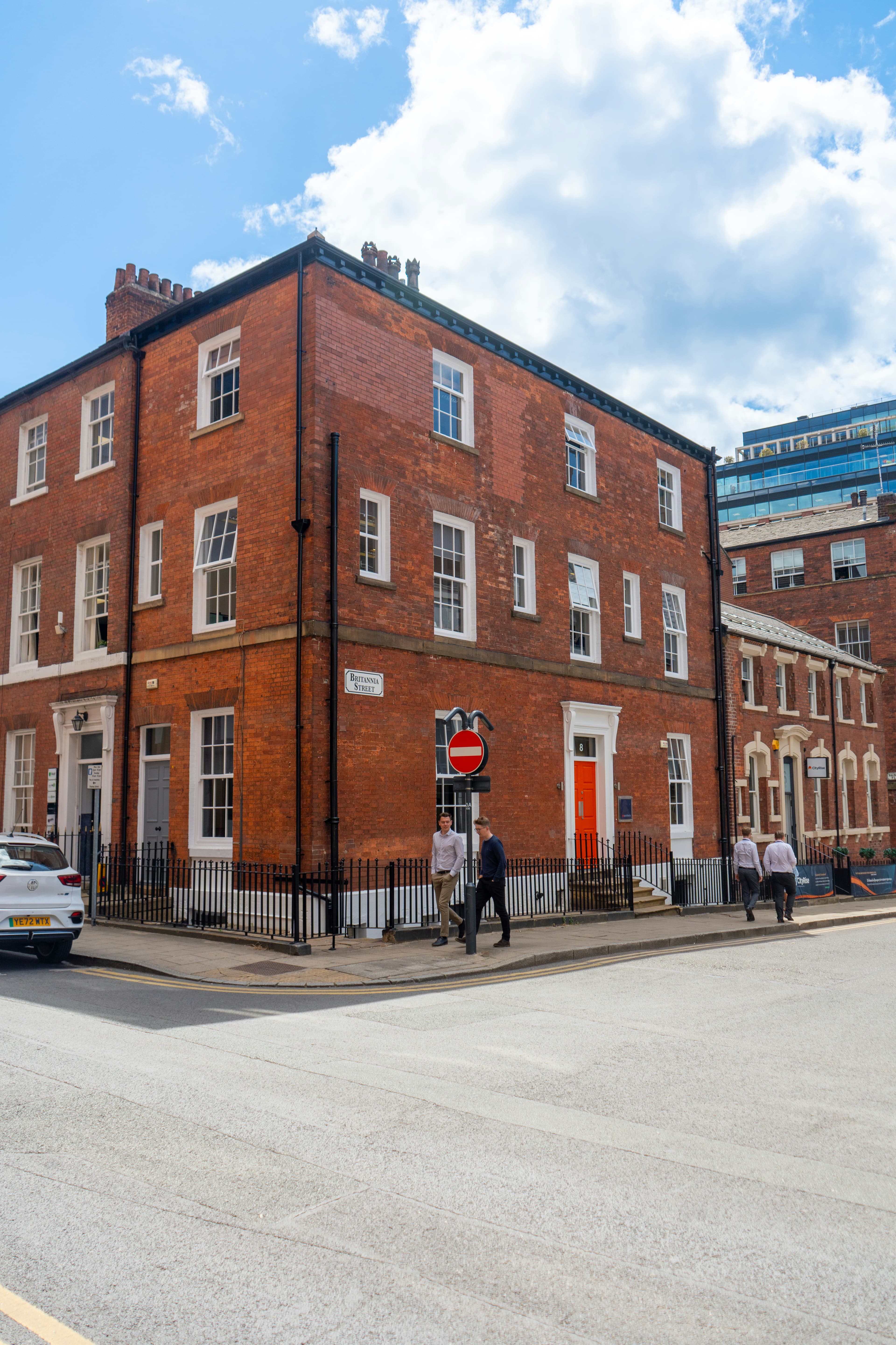 Red brick corner building on Britannia Street with white windows and people on the sidewalk.