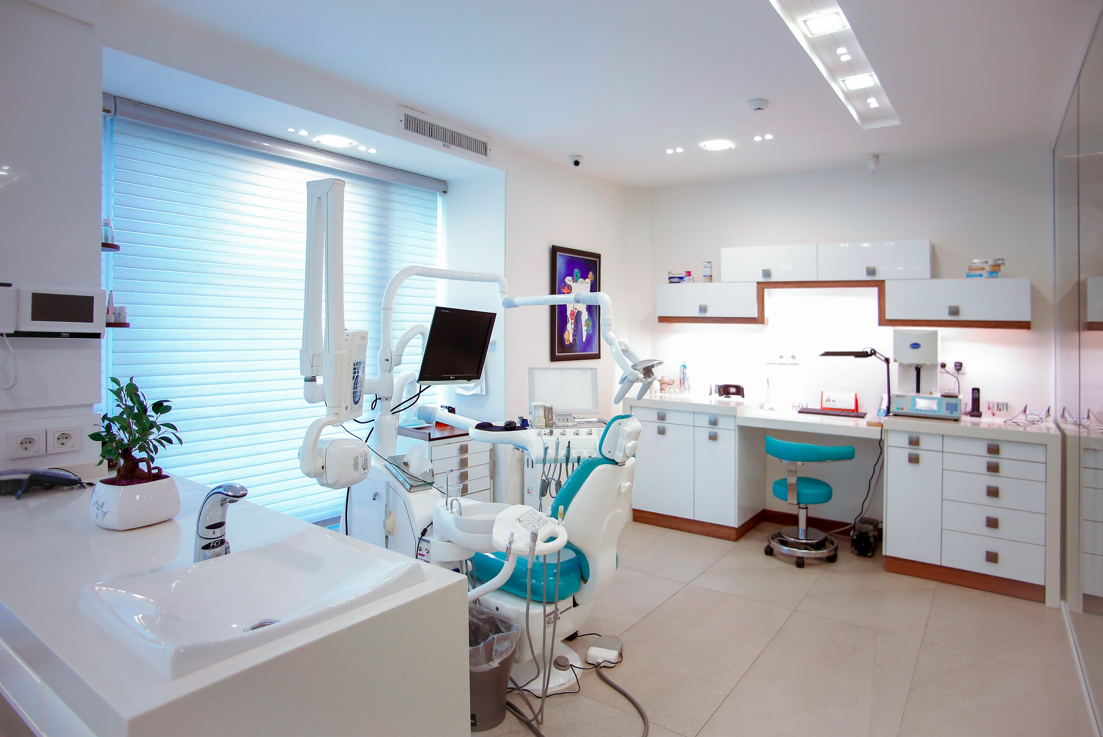 Bright, modern dental office featuring a teal chair, white cabinetry, and advanced medical equipment.