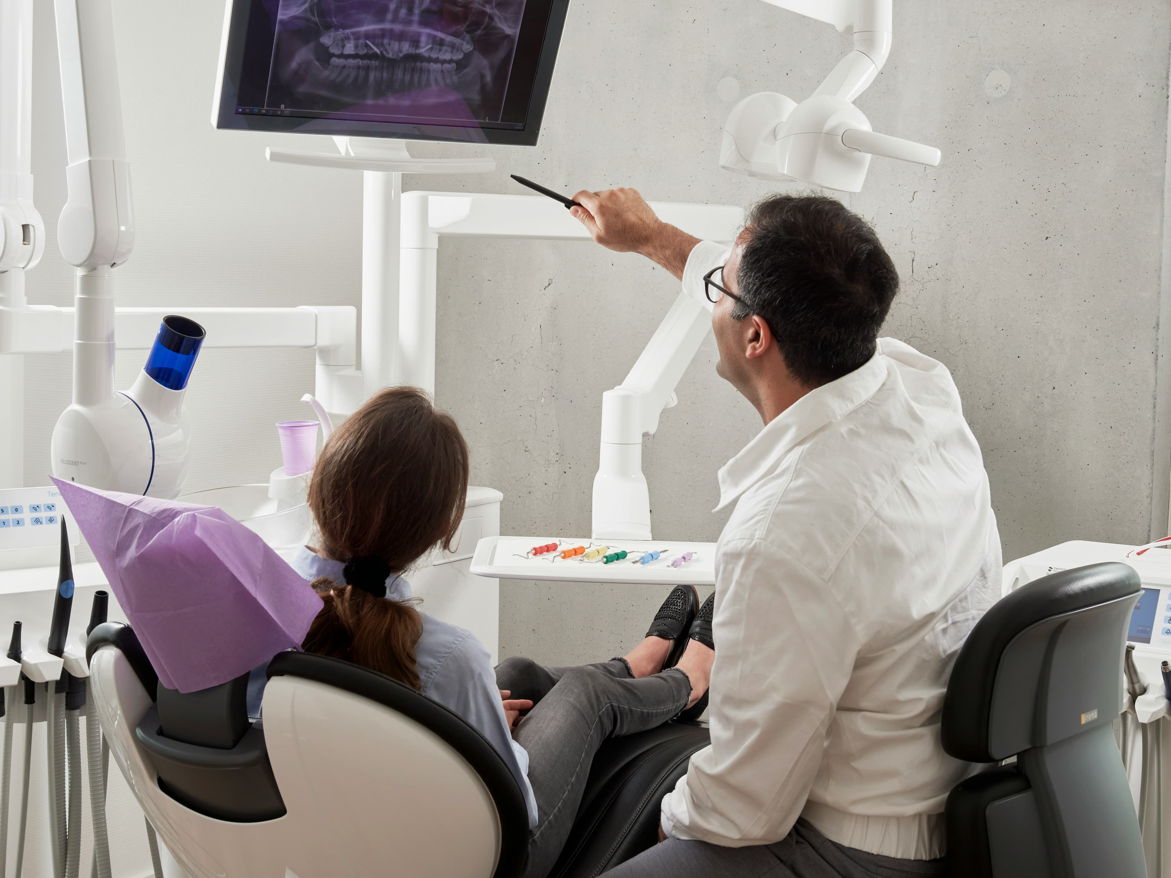 Dentist points to a dental X-ray on a monitor while consulting with a patient.