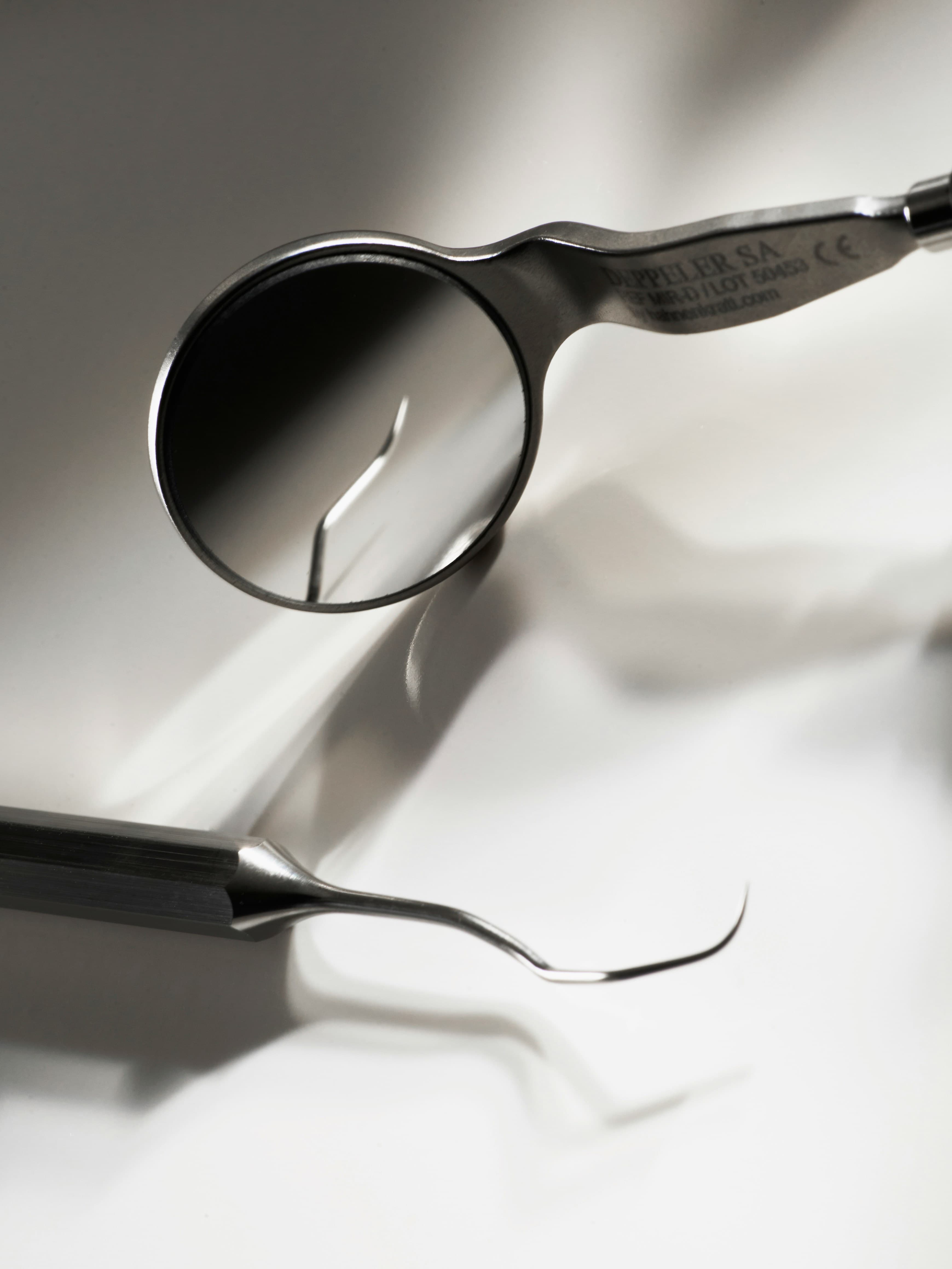 Stainless steel dental mirror reflecting a curved explorer probe on a clean white surface.