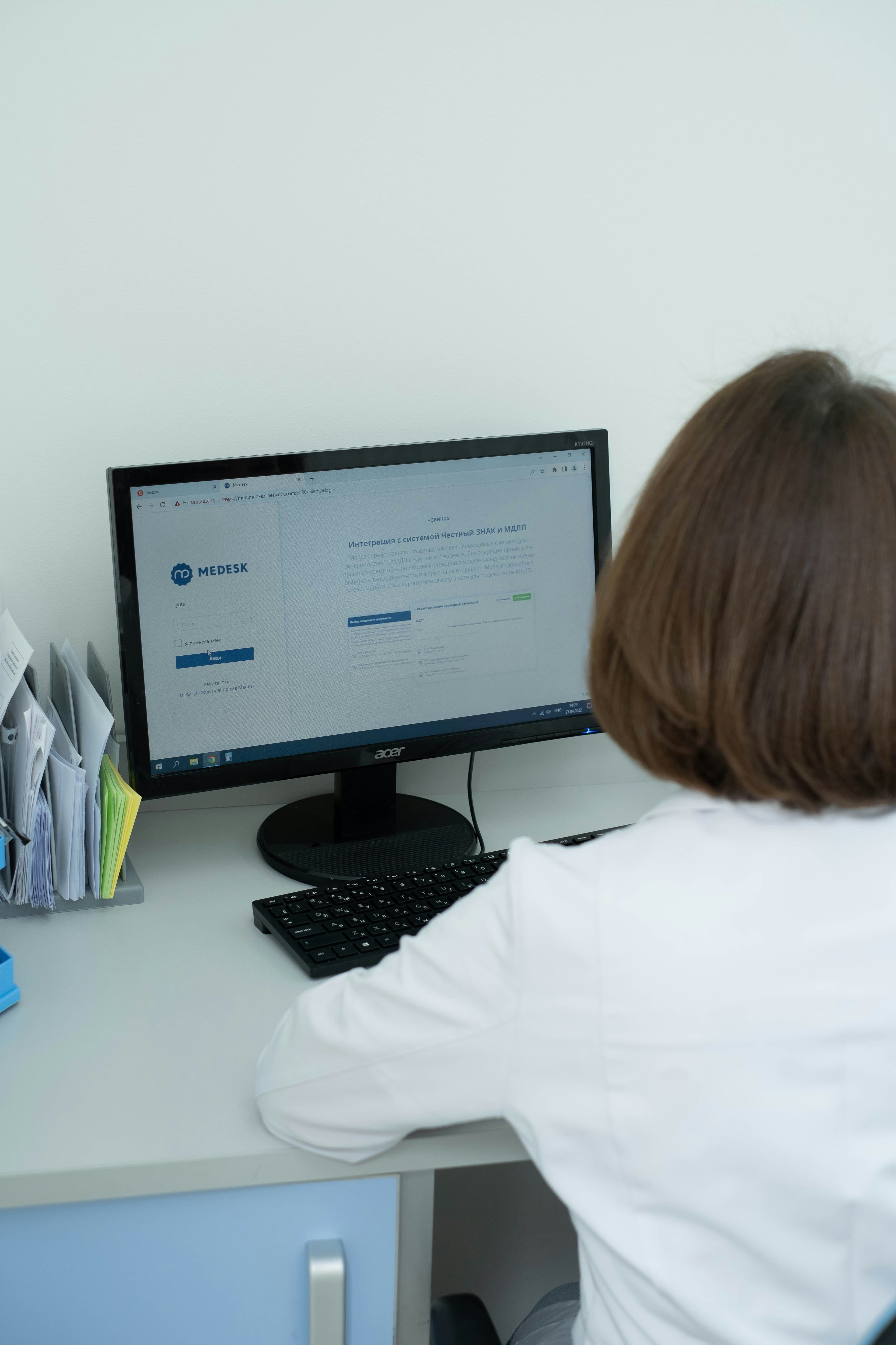Healthcare professional in a white coat viewing a medical software interface on a computer monitor.