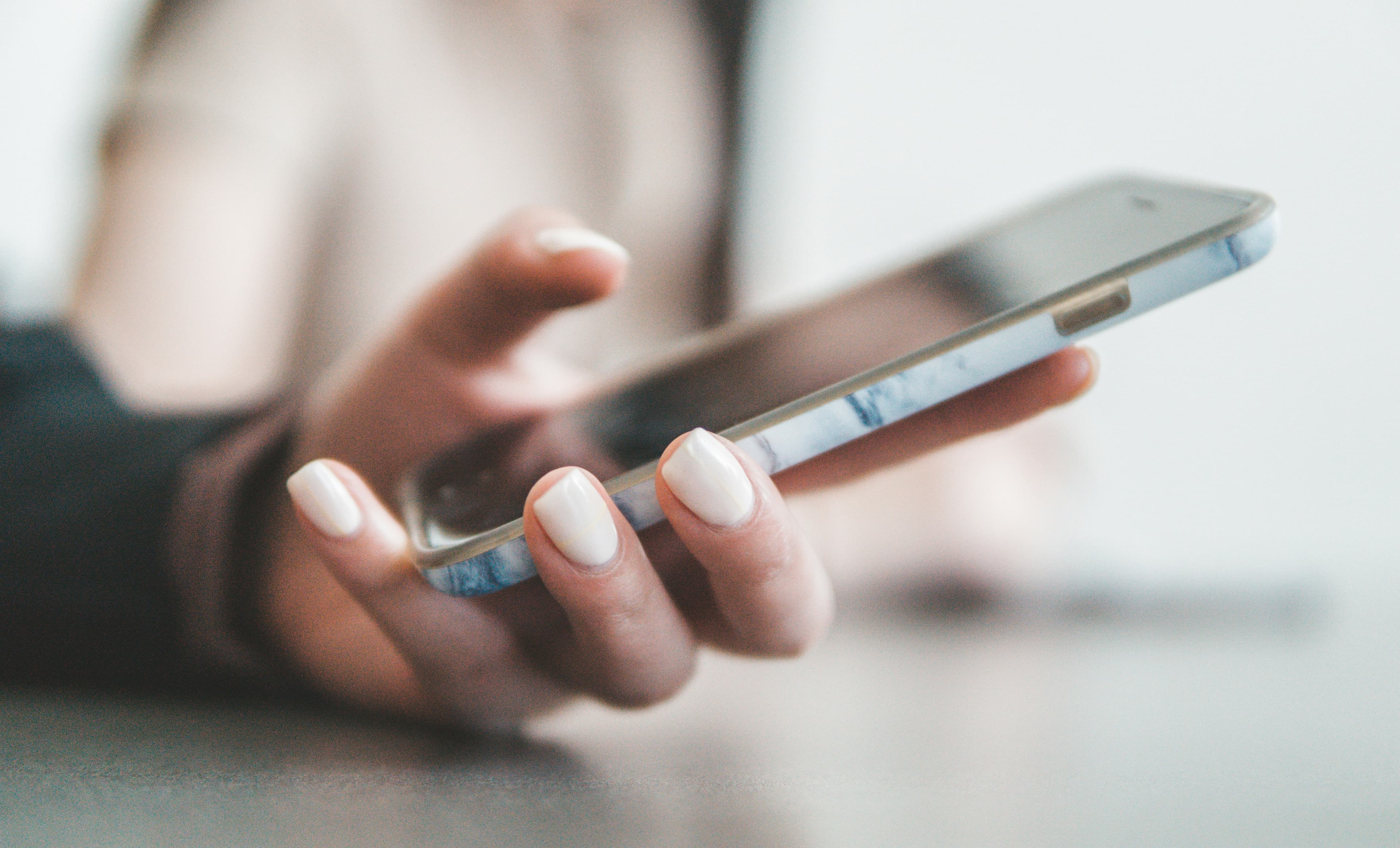 Hand with white manicured nails holding a smartphone with a blue marble patterned case.