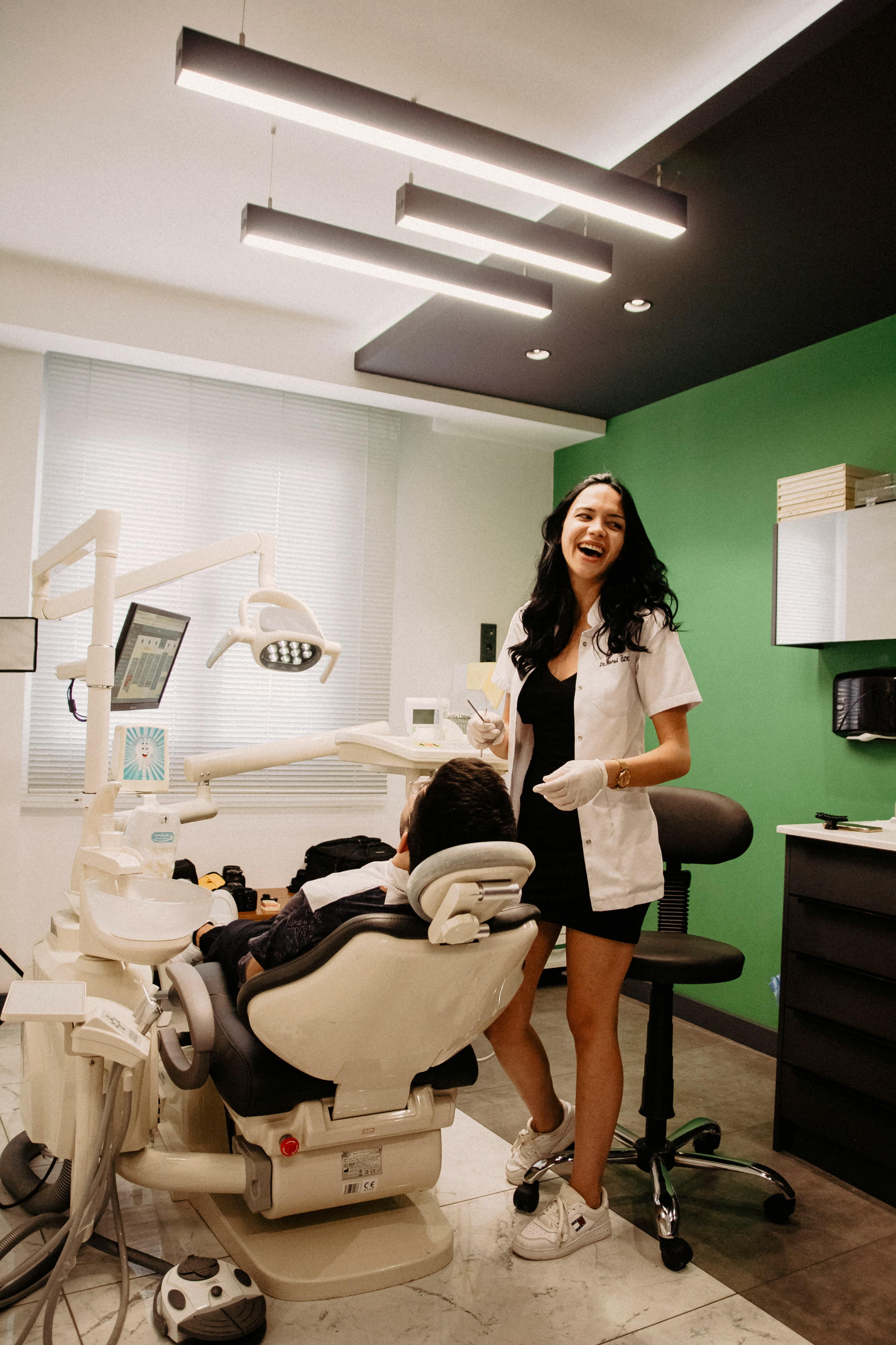 A cheerful female dentist laughs while attending to a patient in a dental chair.